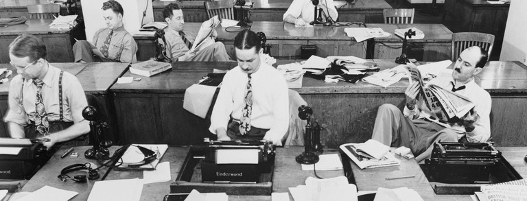 Das Bild zeigt ein Großraumbüro. Menschen arbeiten an Schreibmaschinen und telefonieren.